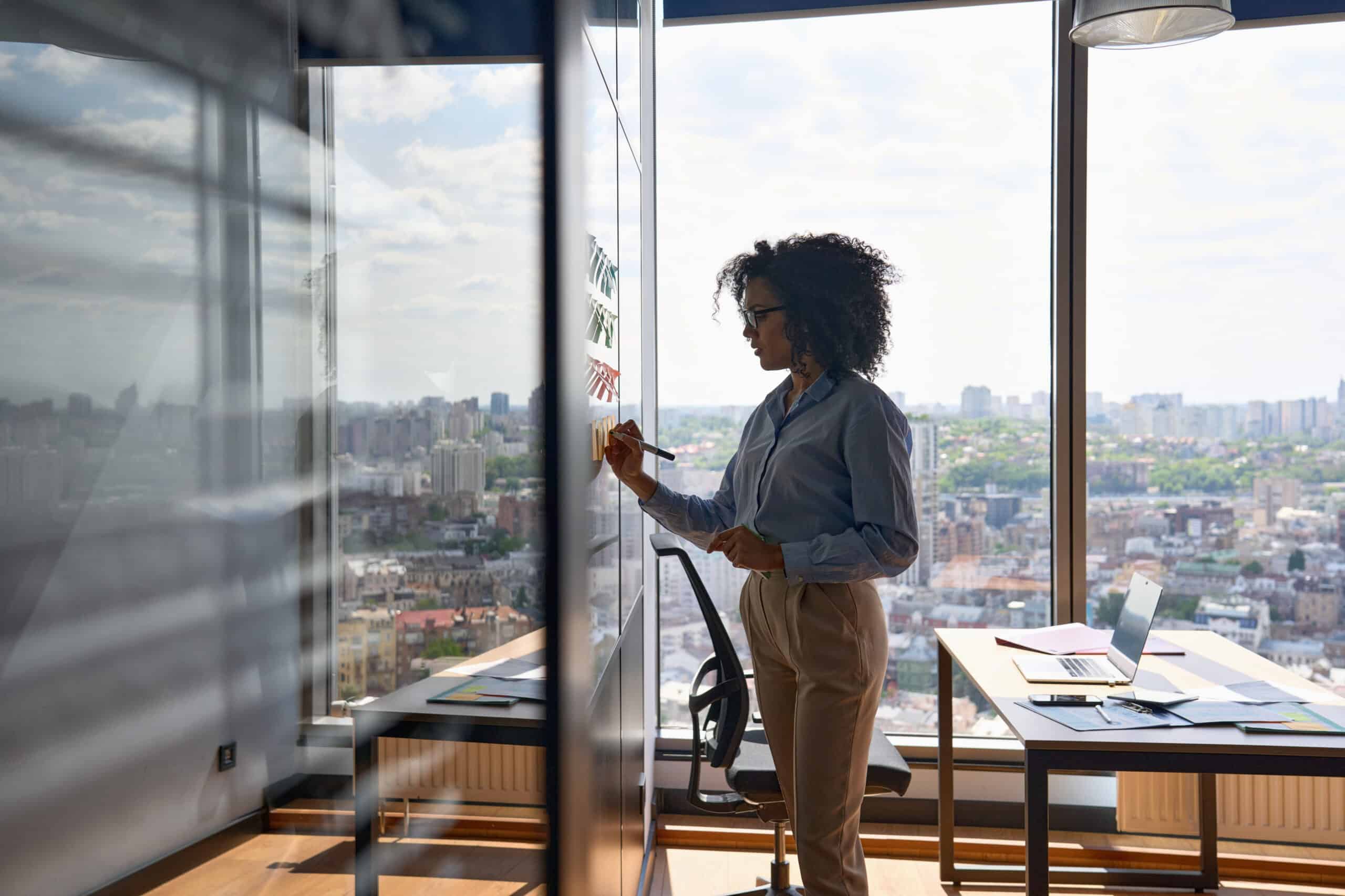 Afro American ceo writing on sticky notes in office with big city urban view.
