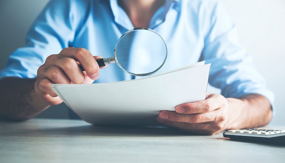 Person looking at papers through magnifying glass